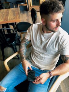 Model sitting in the Worm has Turned bar holding mobile wearing Natural Influence S t-shirt